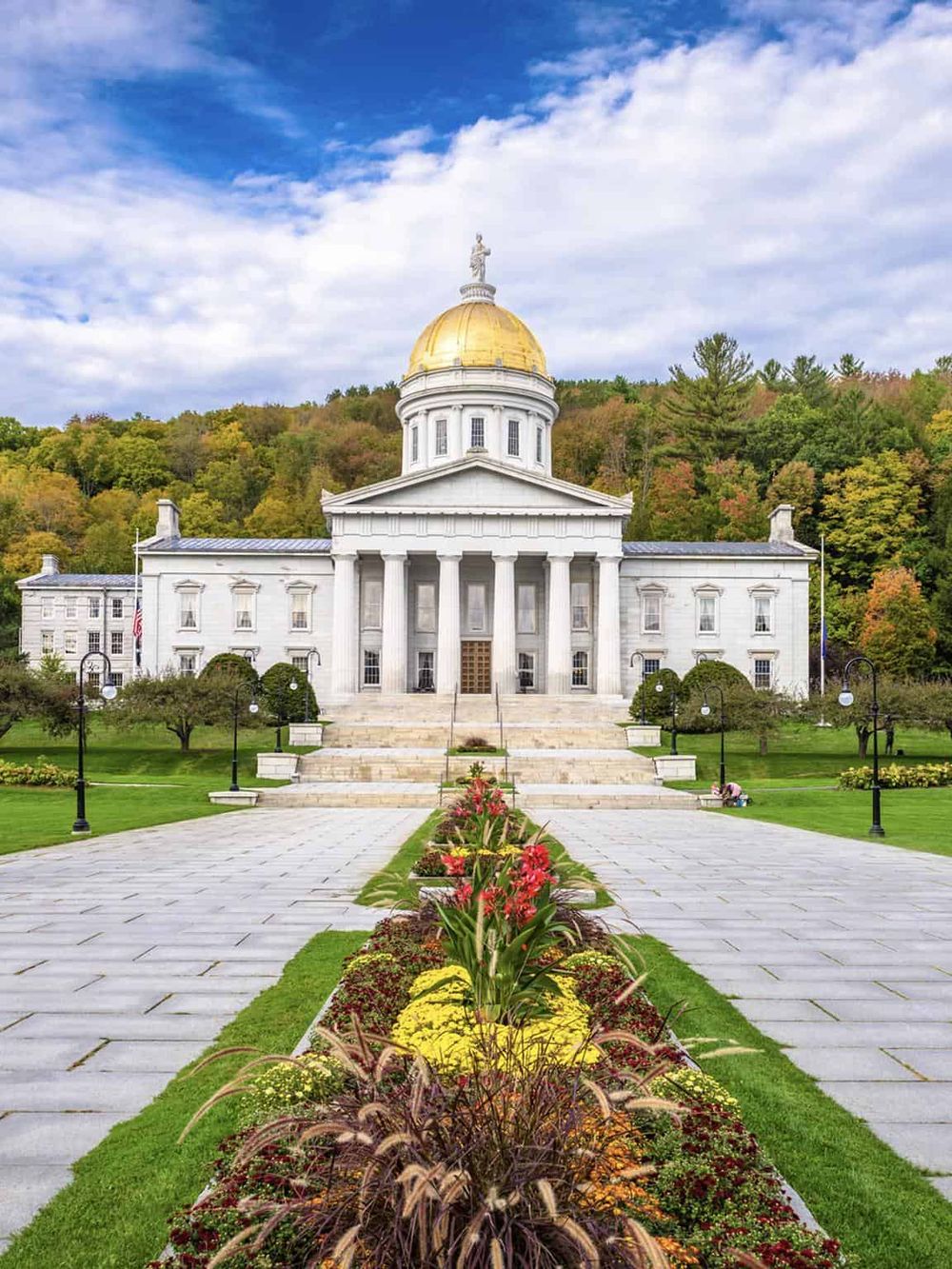Elegant government building with golden dome, surrounded by colorful fall foliage and manicured gardens.