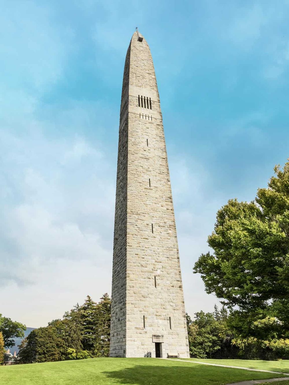 Giant stone obelisk tower with blue sky and greenery, historical landmark in Portland.