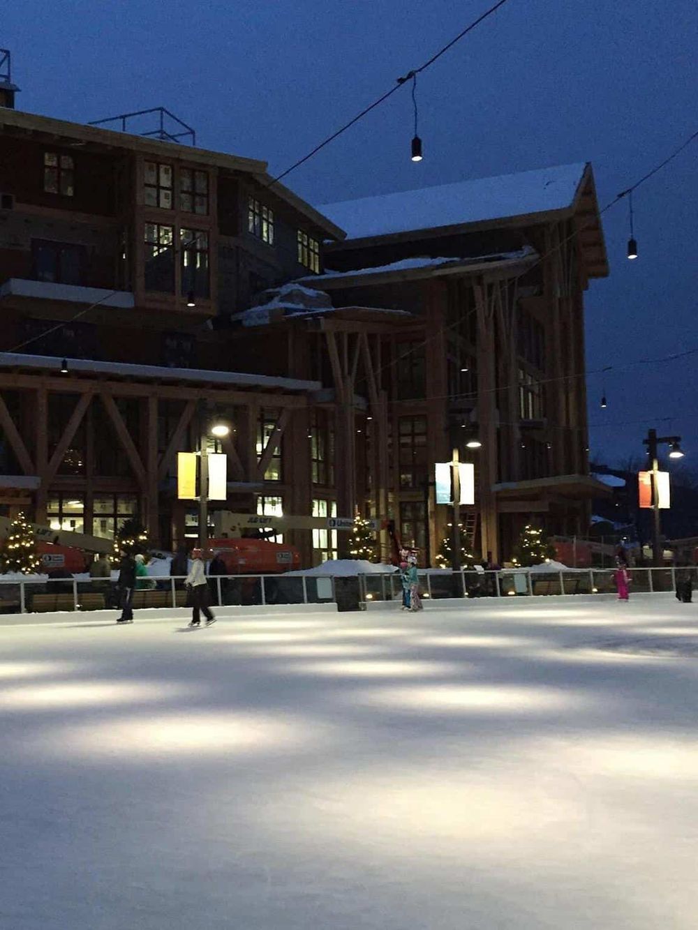 Cozy mountain lodge near ice skating rink at dusk, winter snow scene, festive holiday atmosphere, QuestForDirections.