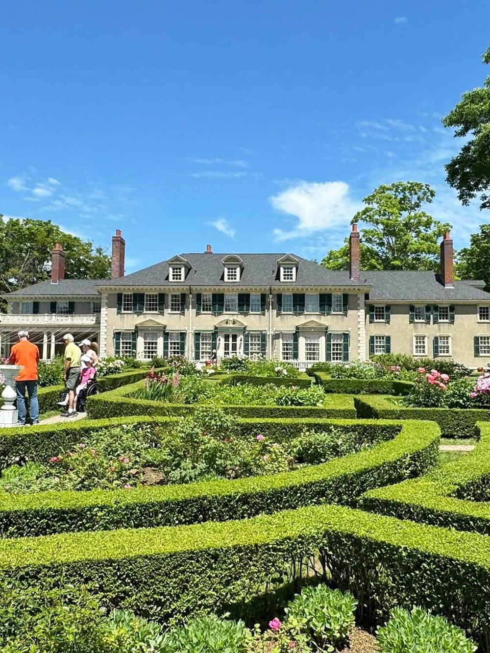 Elegant historic mansion with manicured gardens and visitors enjoying the scenic surroundings.