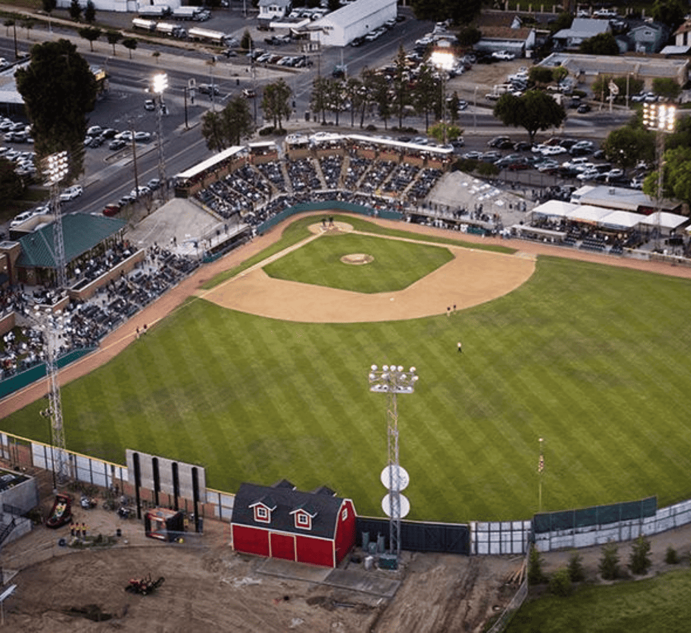 Aerial view of a baseball stadium with lush green field, seating area, and nearby parking lots, showcasing local sports entertainment.