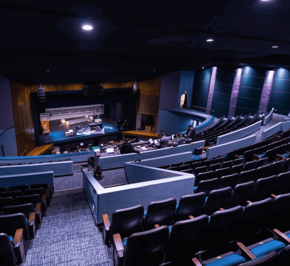 Empty theater auditorium with stage and lighting, preparations underway for a performance or event.