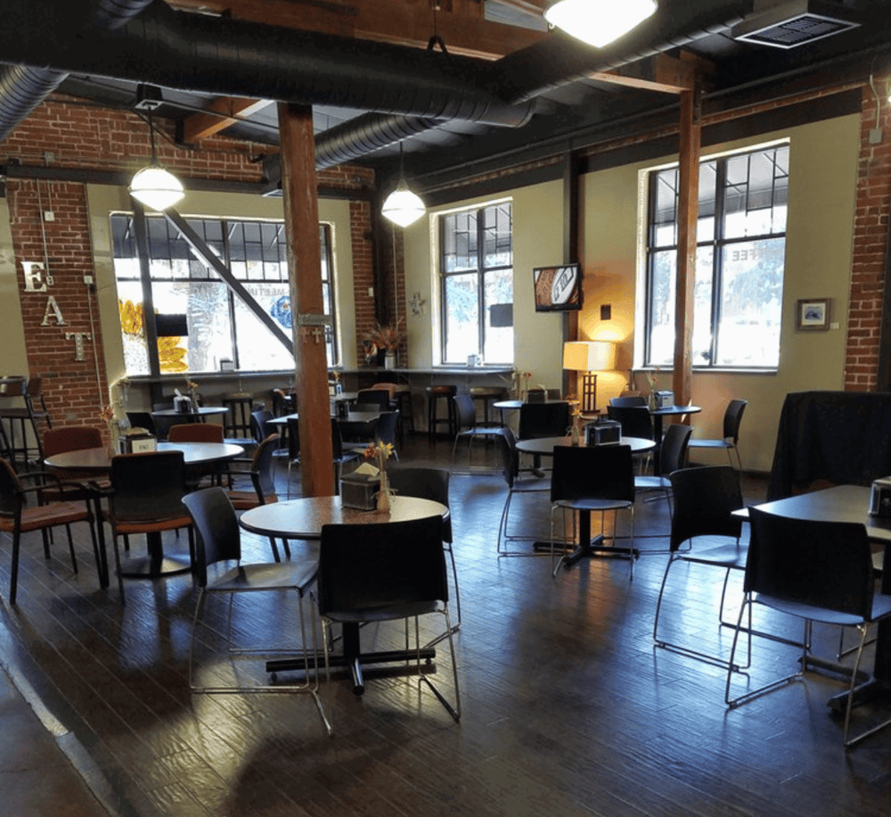 Cozy dining area with rustic brick walls, large windows, and modern black chairs at QuestForDirections.