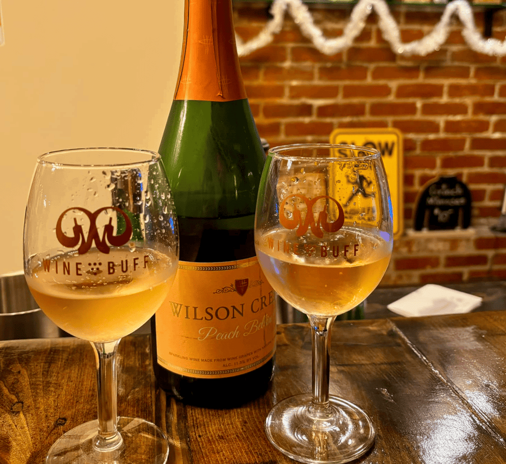 1. Sparkling peach wine in wine glasses with Jameson Wine Buff logo, brick wall background.