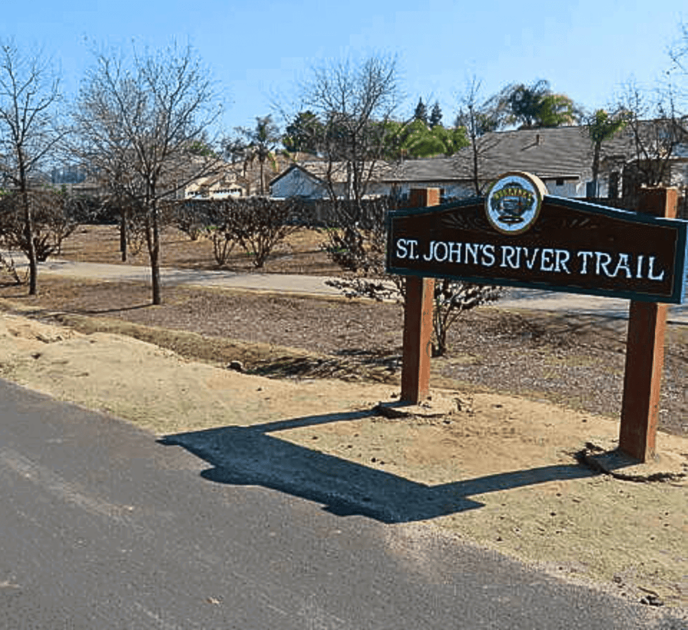 Scenic trail sign for St. John's River Trail in a peaceful neighborhood setting.