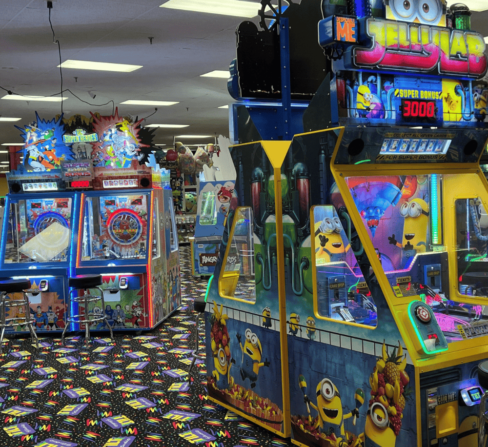 Bright arcade game machines with colorful Minions and superhero themes in an entertainment center.