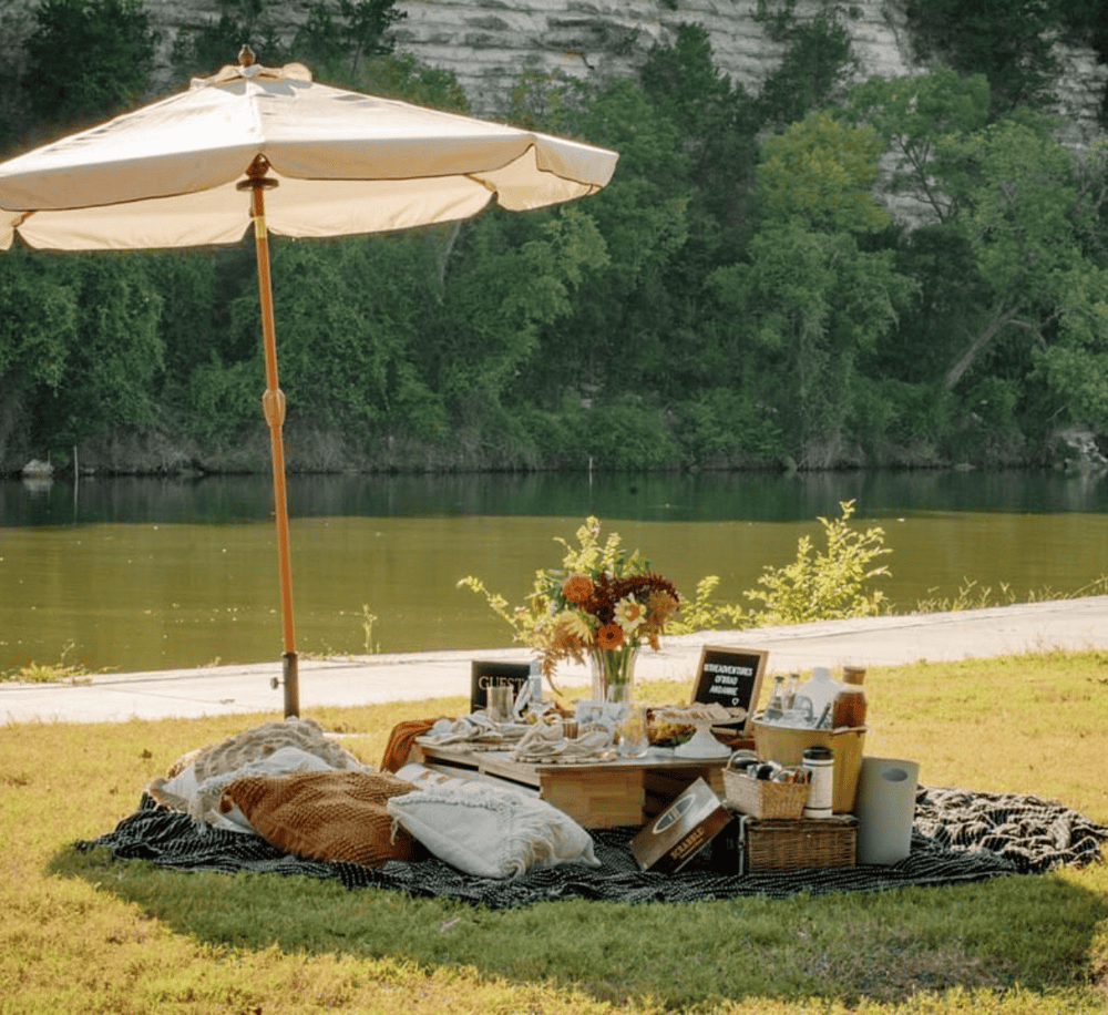 Enjoy outdoor dining by the river with picnic setup, umbrella, and scenic nature views for travel adventures.