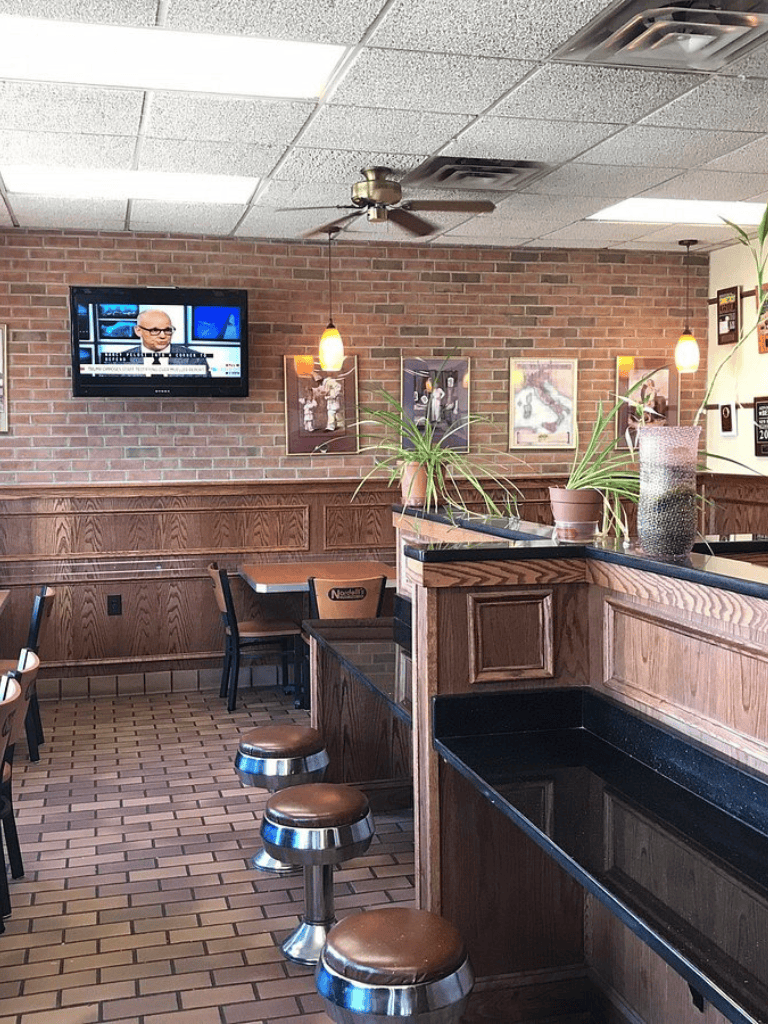 Cozy restaurant interior with brick walls, wall-mounted TV, and wooden furniture.