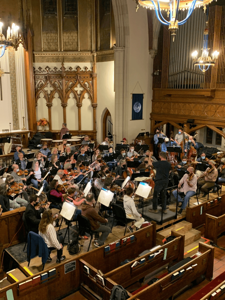 Elegant concert hall with full orchestra rehearsing in historic church setting, vibrant atmosphere for classical music performances.