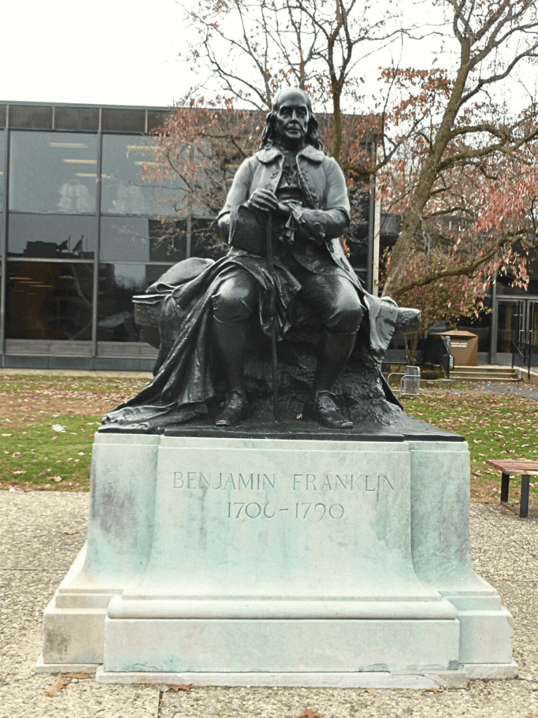 Bronze statue of Benjamin Franklin in a park with trees, historical significance, and outdoor setting.