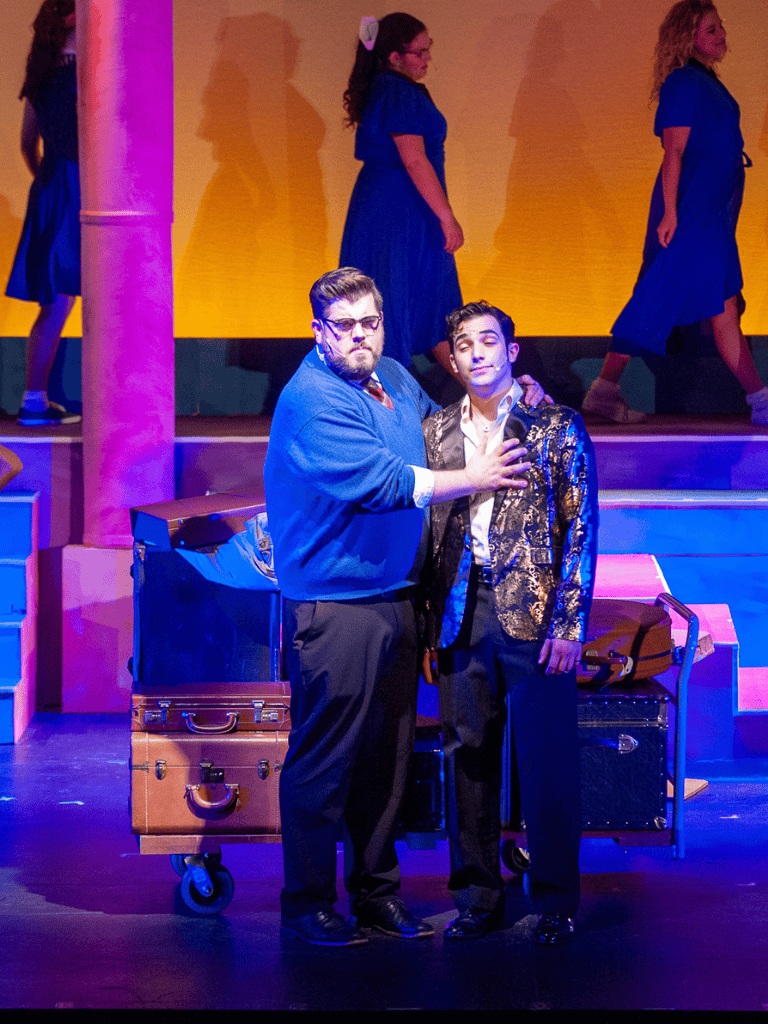 An engaging stage performance featuring actors in colorful costumes with a vibrant background and diverse cast.