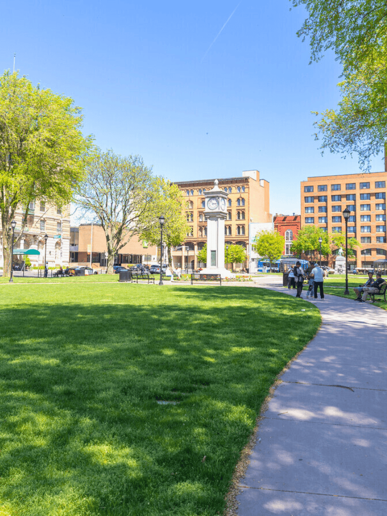 Colorful city park in downtown with green grass, trees, clock tower, and benches, ideal for relaxation and outdoor activities.