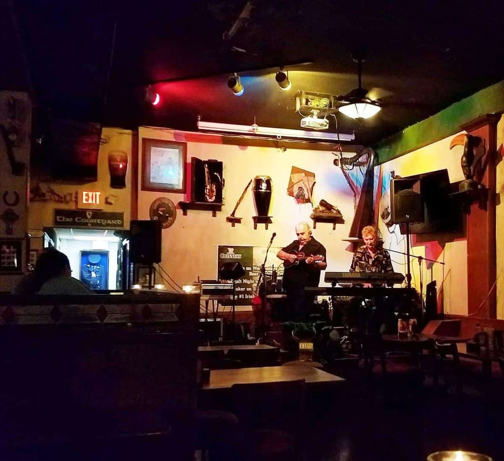 Live music performance at a cozy bar with musicians playing guitar and keyboard, vibrant lighting, and warm ambiance.