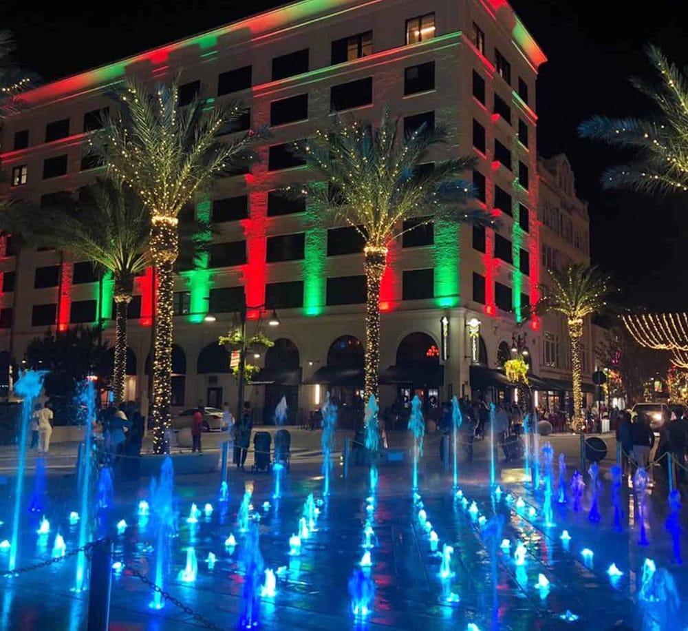 Colorful holiday lights decorating downtown building and illuminated fountain at night.