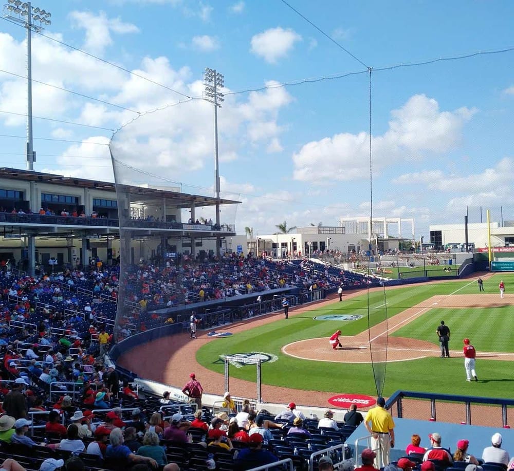 Crowd watching a baseball game at a stadium with blue sky and fluffy clouds.