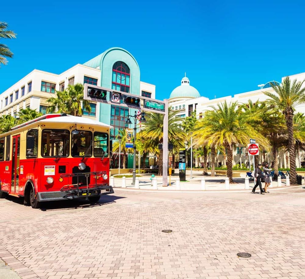 Vintage trolley in front of modern mall with palm trees in sunny urban setting.