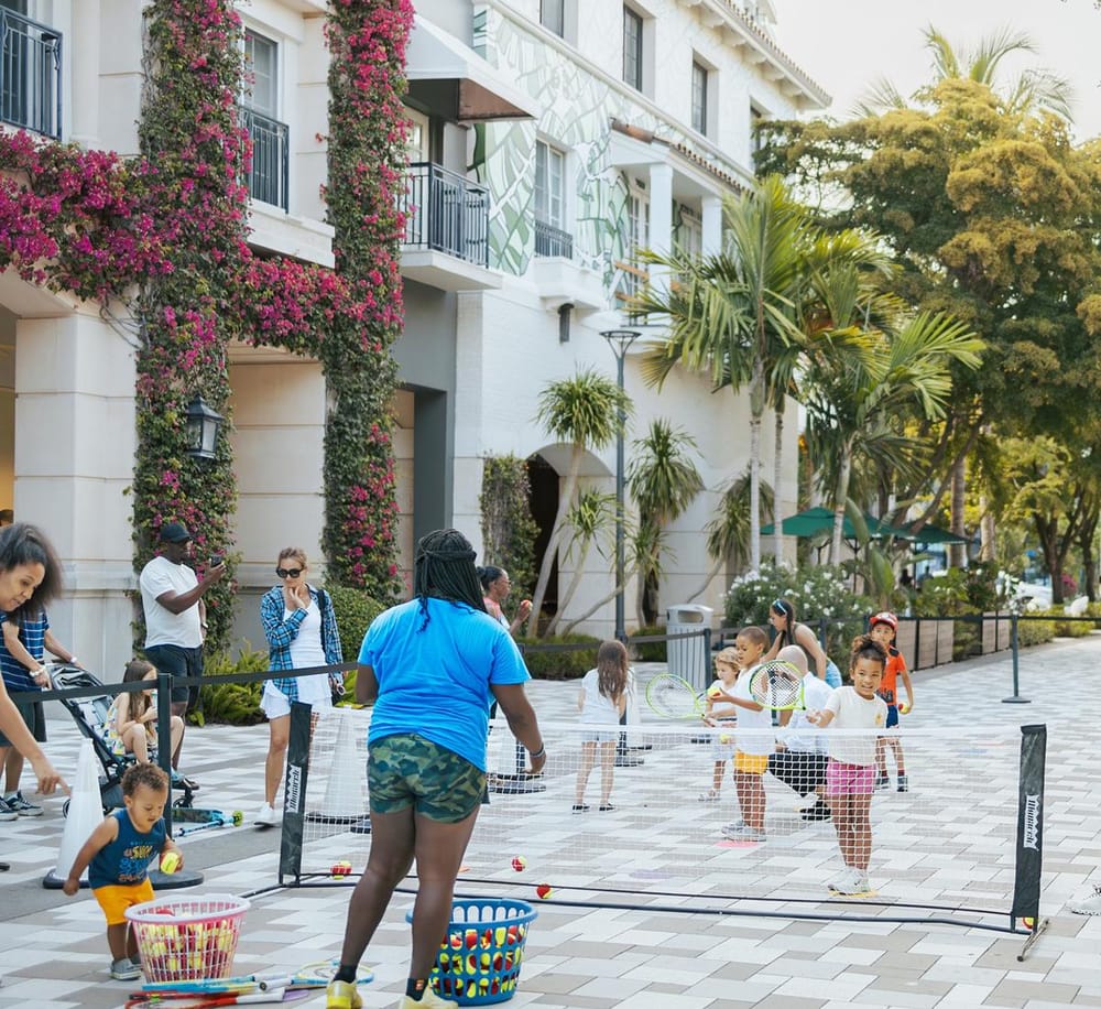 Kids playing tennis at outdoor court in vibrant urban setting.