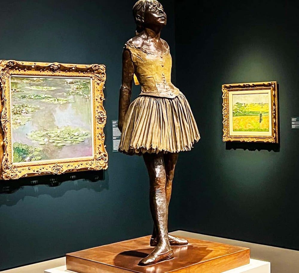 1. Bronze sculpture of a girl in a yellow dress in art museum surrounded by paintings.