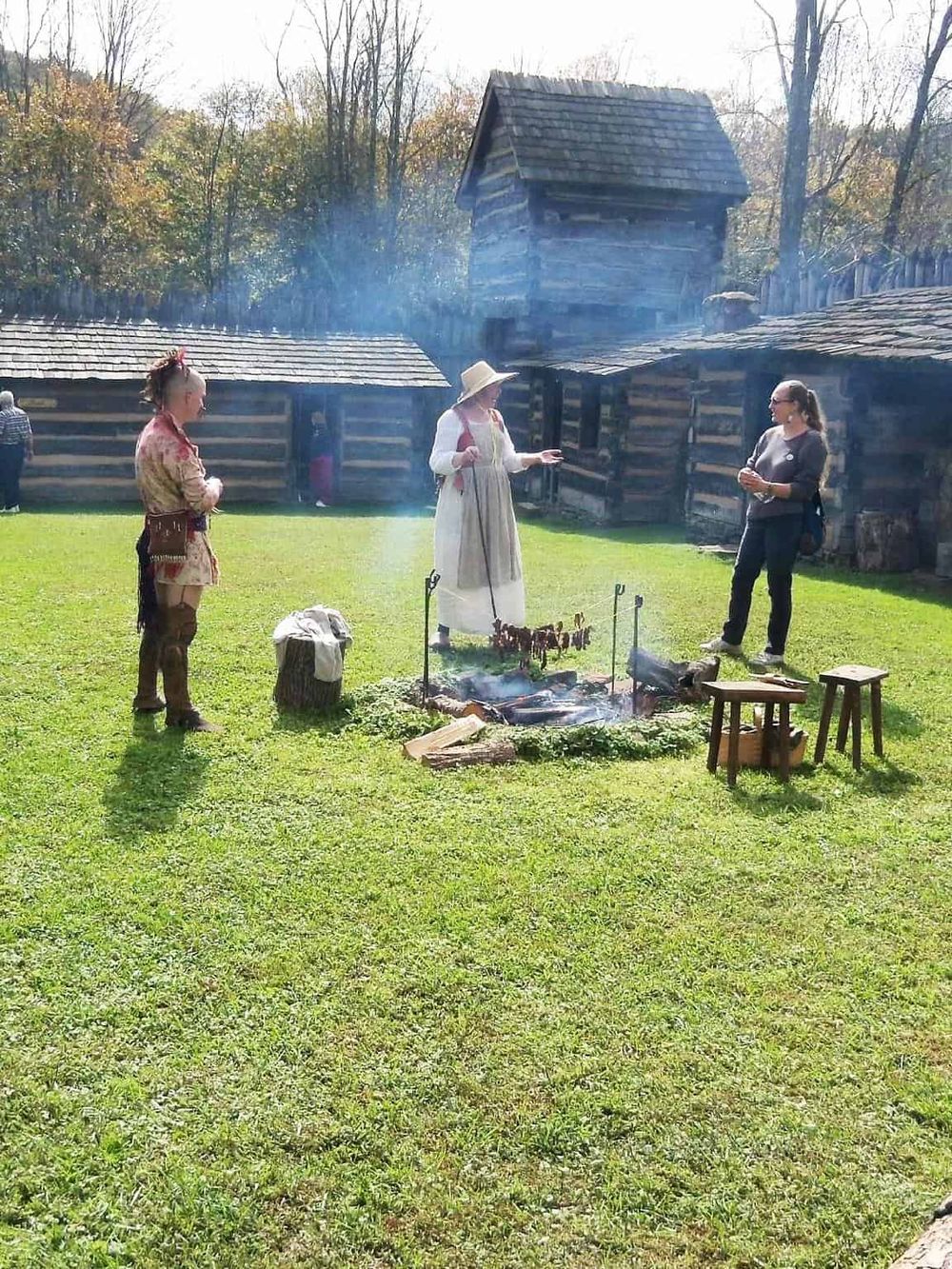 Outdoor historical reenactment at an open-air museum showcasing pioneer life, traditional cooking methods, and 19th-century log cabins.
