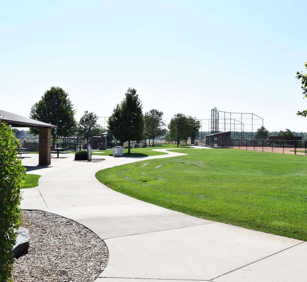 Spacious outdoor park with walking paths, trees, playground, and sports fields for community recreation.