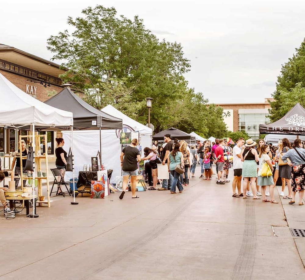 Outdoor artisan craft fair with vendor tents and visitors shopping.
