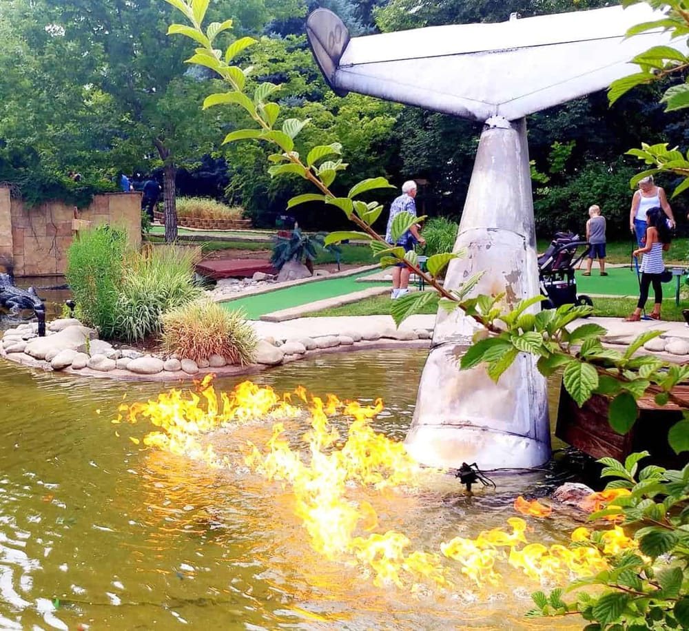Colorful mini golf course with a flaming water feature and lush greenery at QuestForDirections.