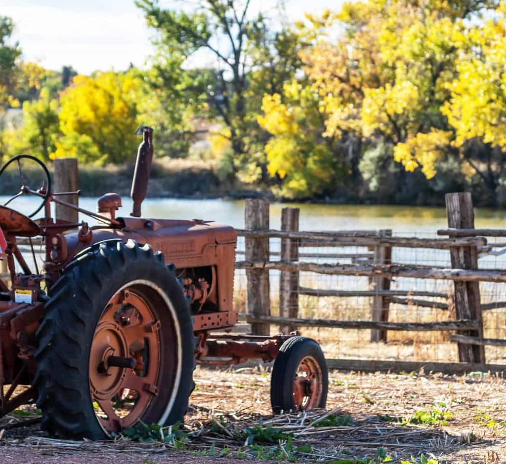 Rustic tractor by the river in fall with colorful trees, ideal for rural travel and outdoor adventure SEO.