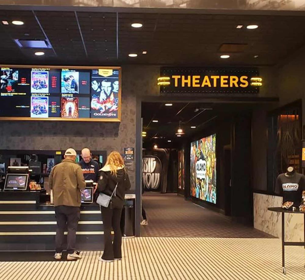 Bright movie theater ticket counter with digital display and "Theaters" sign, welcoming moviegoers for entertainment.