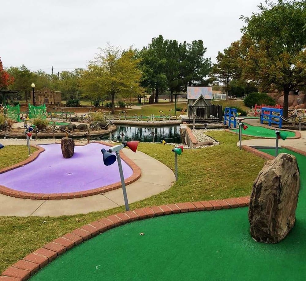 Colorful mini golf course in a park setting with trees and water features, perfect for family fun and outdoor recreation.
