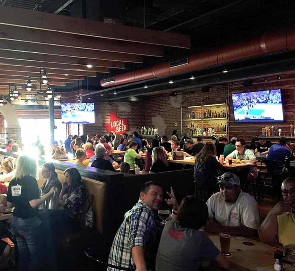 Vibrant bar and restaurant atmosphere with patrons watching sports on TVs, showcasing a lively social dining experience.