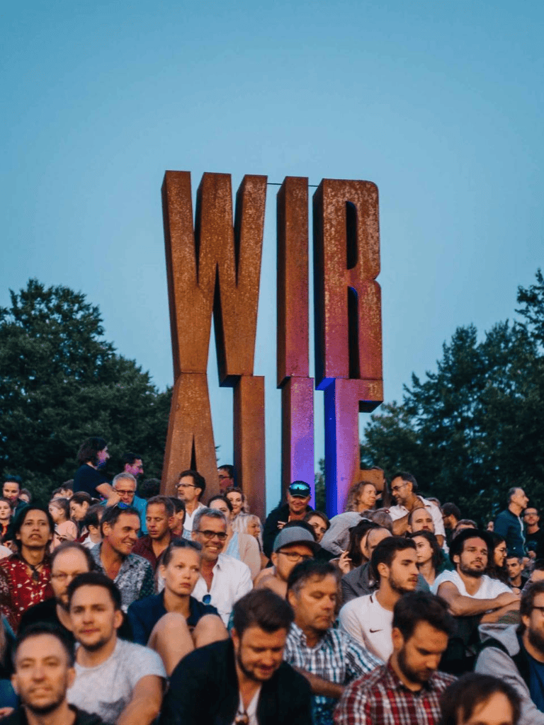 WIR large outdoor event with diverse crowd and giant WIR sculpture during sunset.