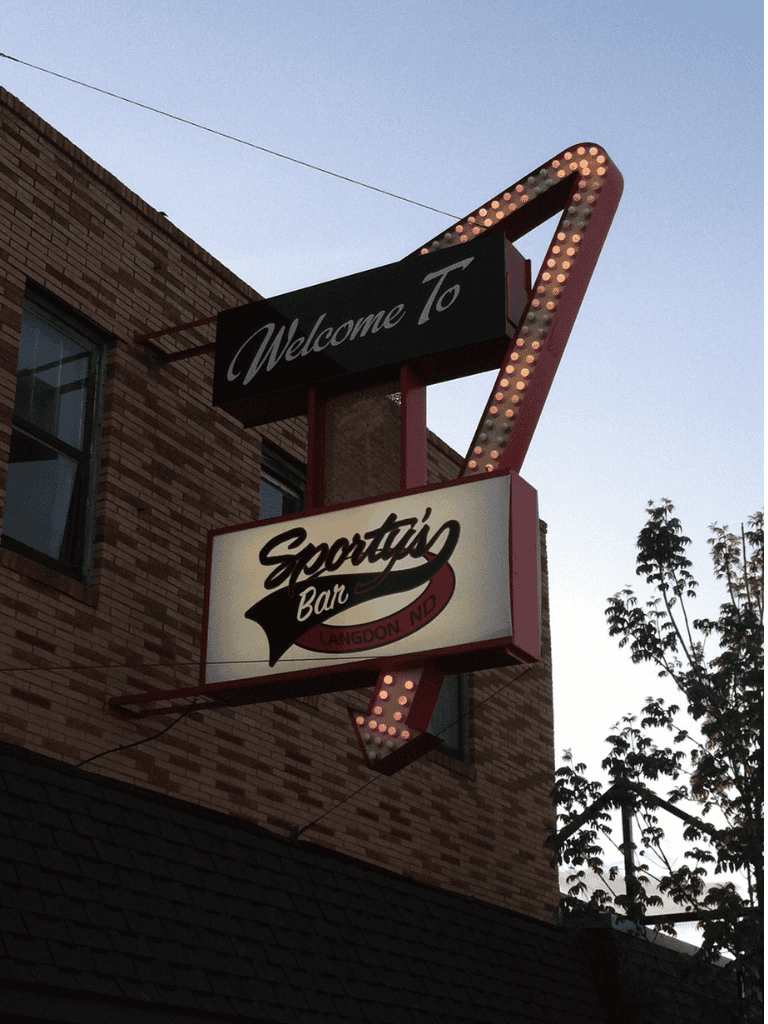 Welcoming sign for Sporting Bar in Laneadon, Oregon, illuminated at dusk.
