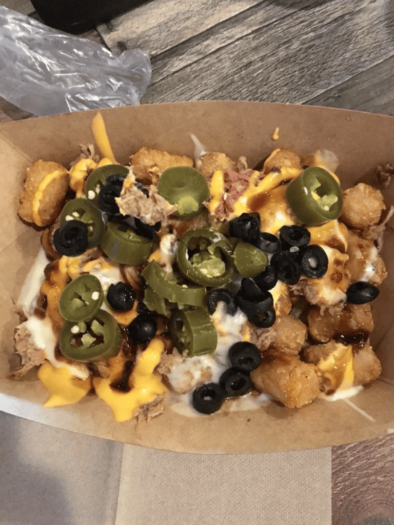 Spicy loaded fries with jalapenos, black olives, melted cheese, and crispy chicken bites on paper tray.