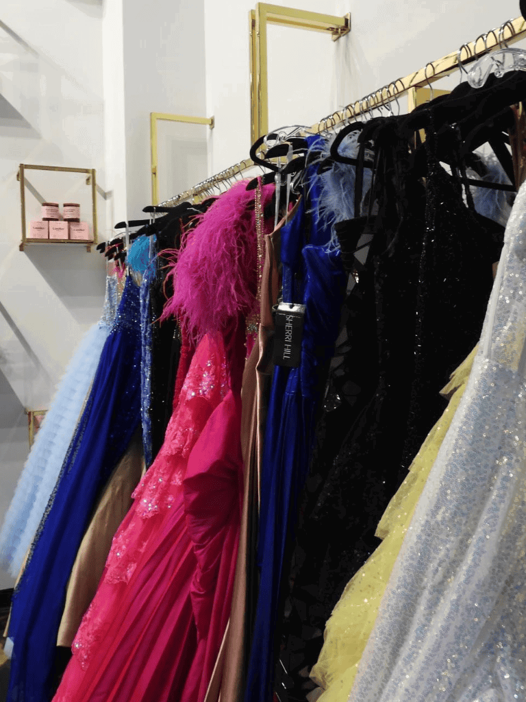 Elegant prom dresses on a clothing rack in a boutique store, showcasing colorful and sparkly formal gowns.