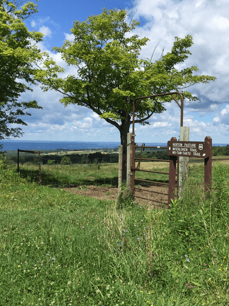 Trail sign at Horton Pasture with scenic landscape and blue sky.