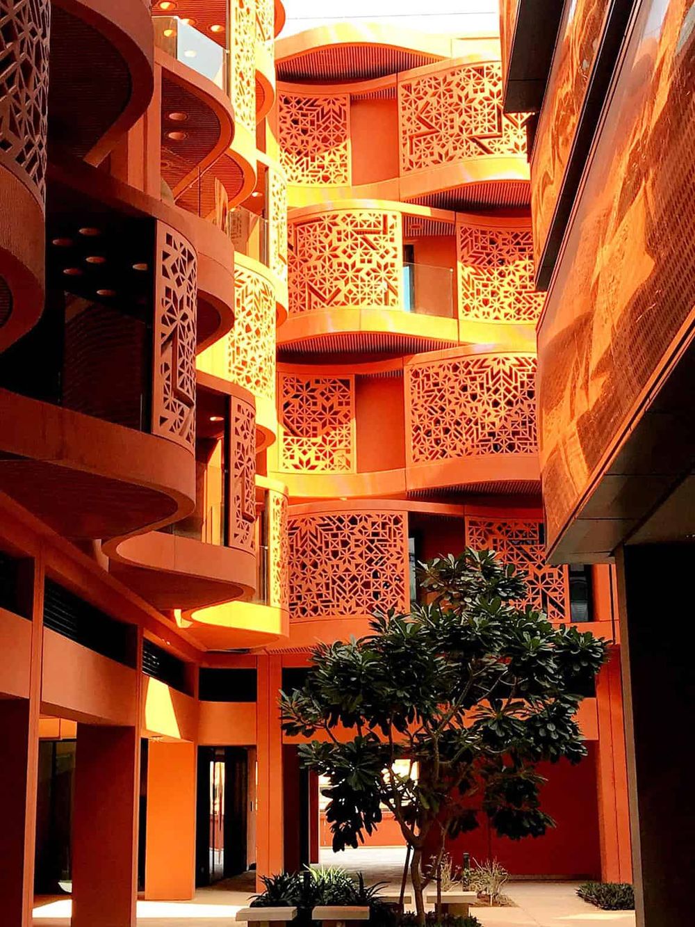 Vibrant orange modern hotel with intricate lattice balconies and lush landscaping, perfect for destination travel.