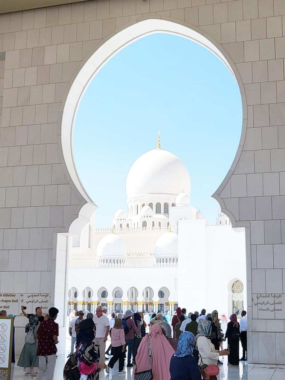 Stunning view of Sheikh Zayed Grand Mosque in Abu Dhabi framed by a decorative archway, showcasing Islamic architecture and a vibrant visitor crowd.