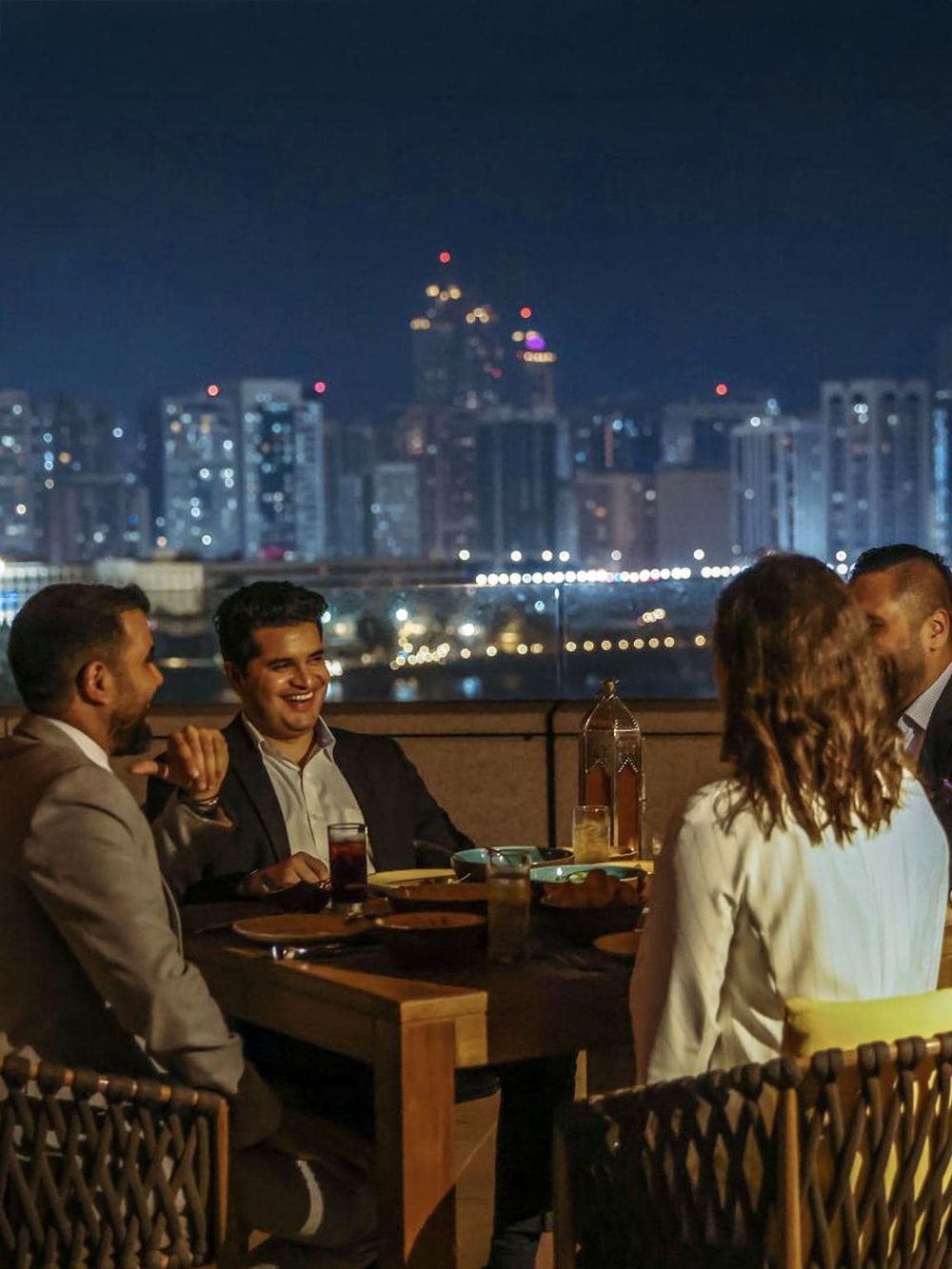 Night city skyline view from rooftop restaurant with business people dining and socializing.