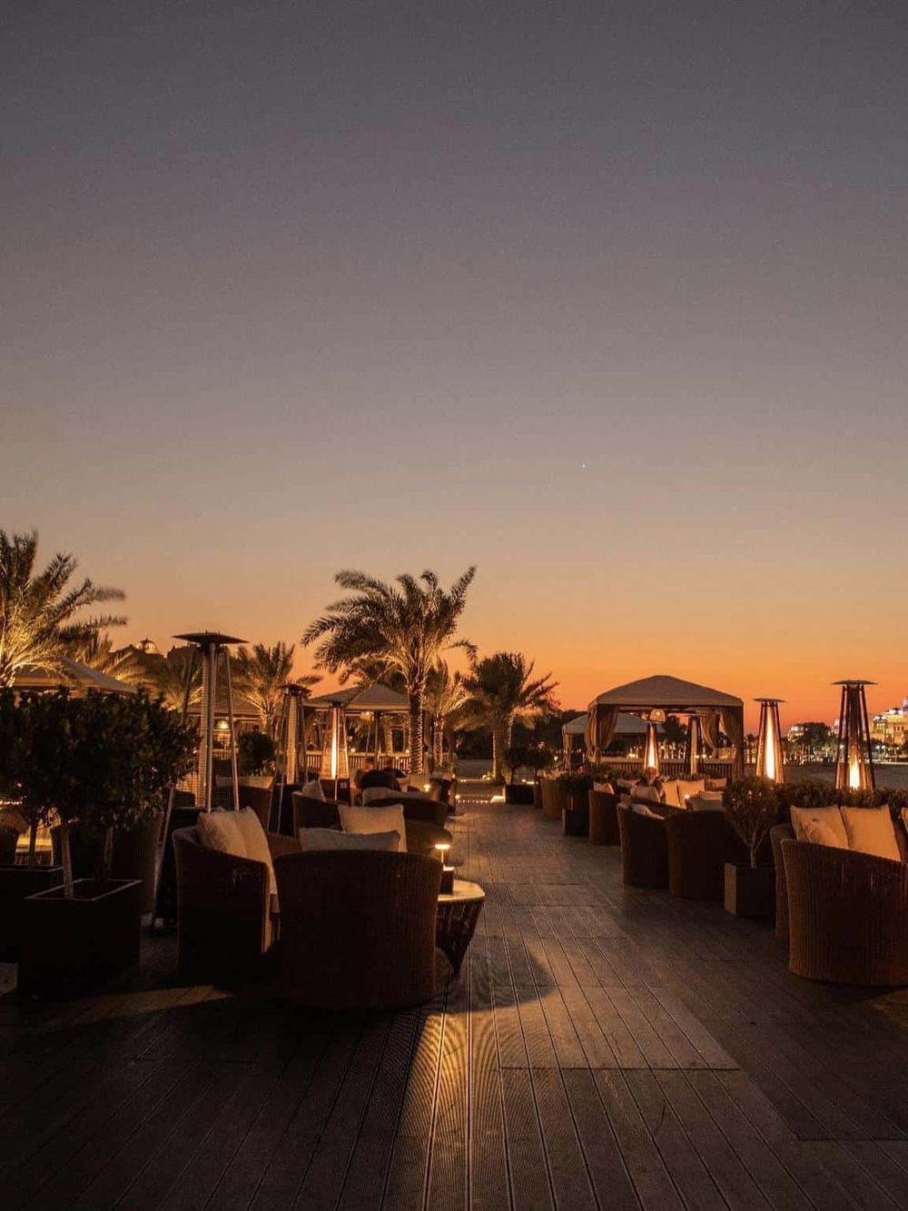 Outdoor lounge area at sunset with palm trees and cozy seating, perfect for relaxation and scenic views.