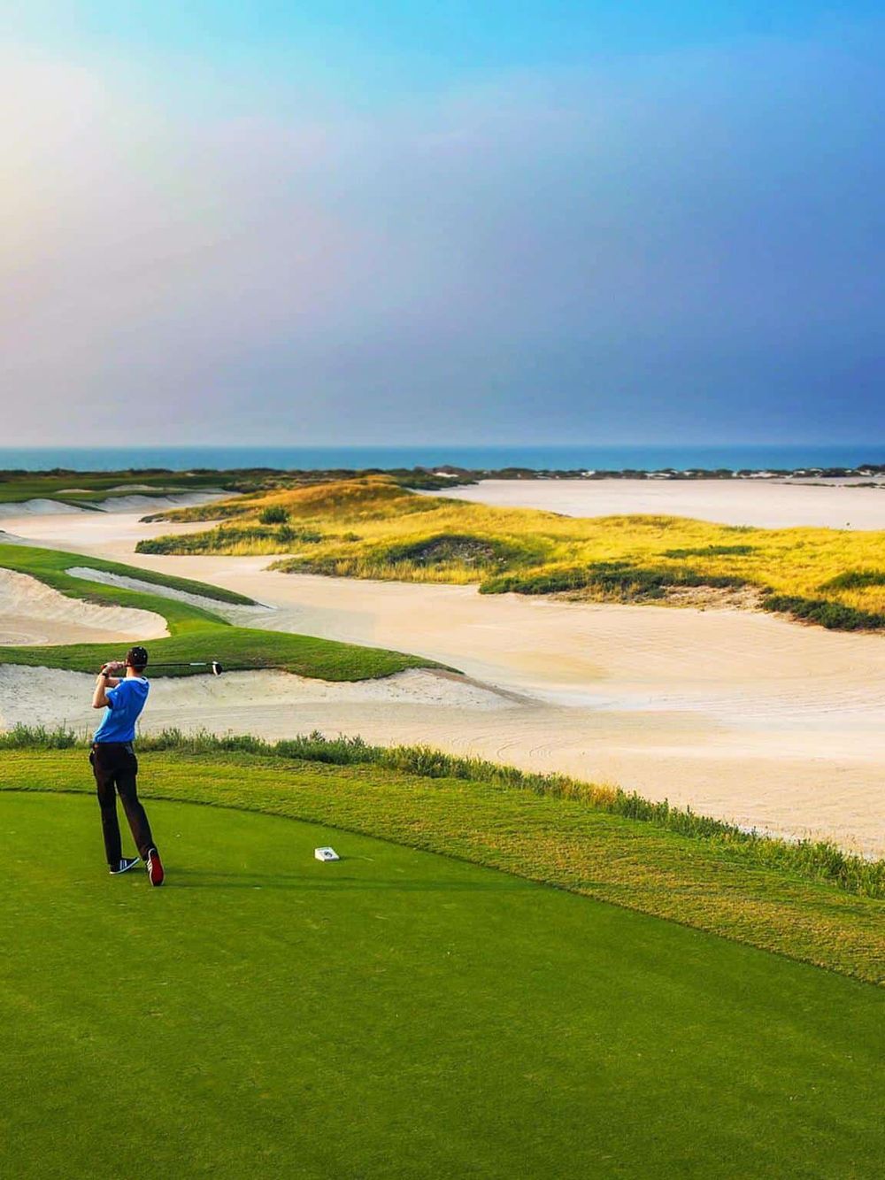 Vibrant golf course near the beach with a golfer teeing off under a colorful sky, perfect for a scenic golf retreat.