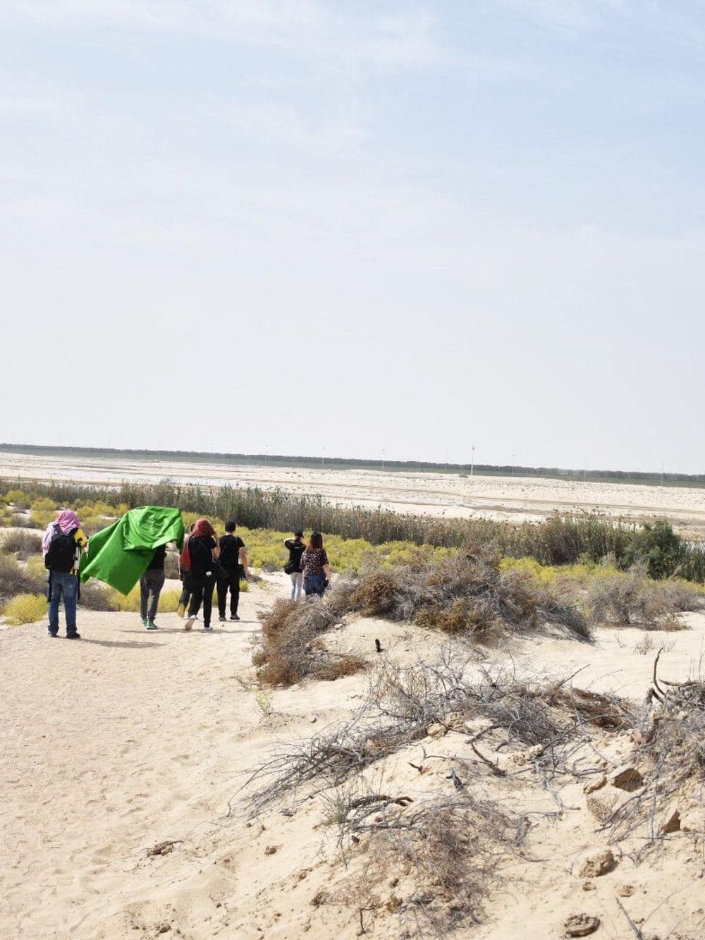 Hiking group walking through sandy dunes with sparse vegetation, desert landscape, clear sky, outdoors, adventure, exploration, QuestForDirections.
