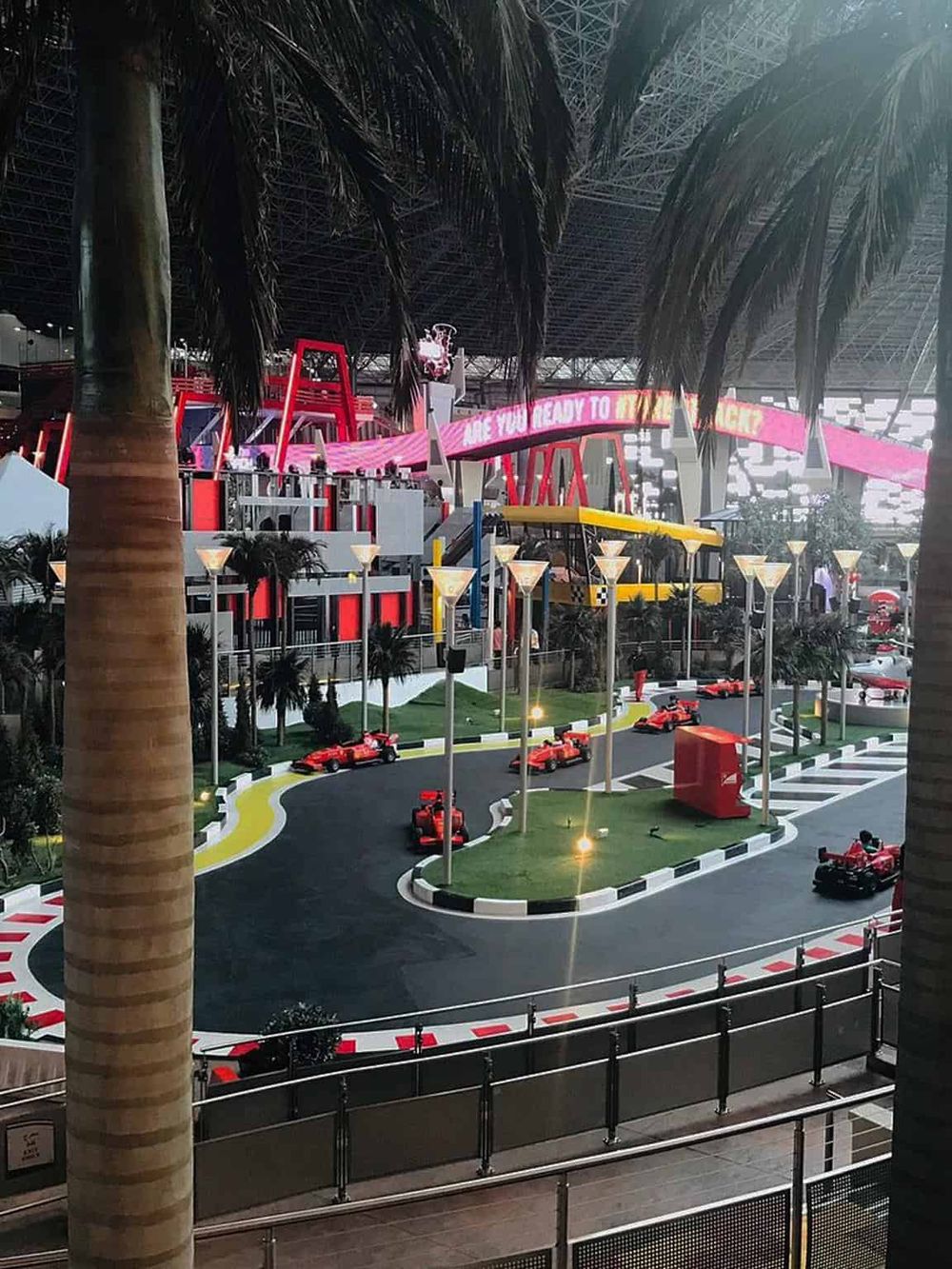 Indoor go-kart race track with colorful cars, palm trees, and vibrant lighting at QuestForDirections.
