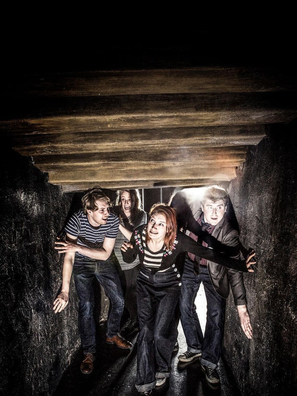 Struggling group of friends in a dark underground tunnel, emphasizing adventure and mystery.