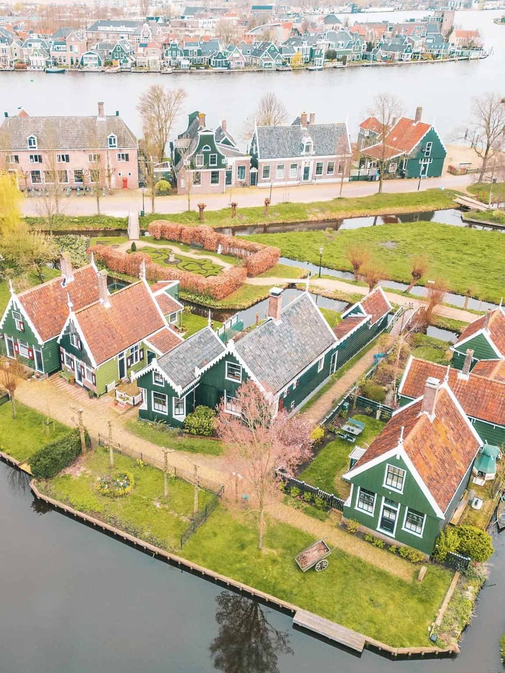 Vibrant green Dutch-style houses near water in a picturesque neighborhood with floral gardens and serene waterways.