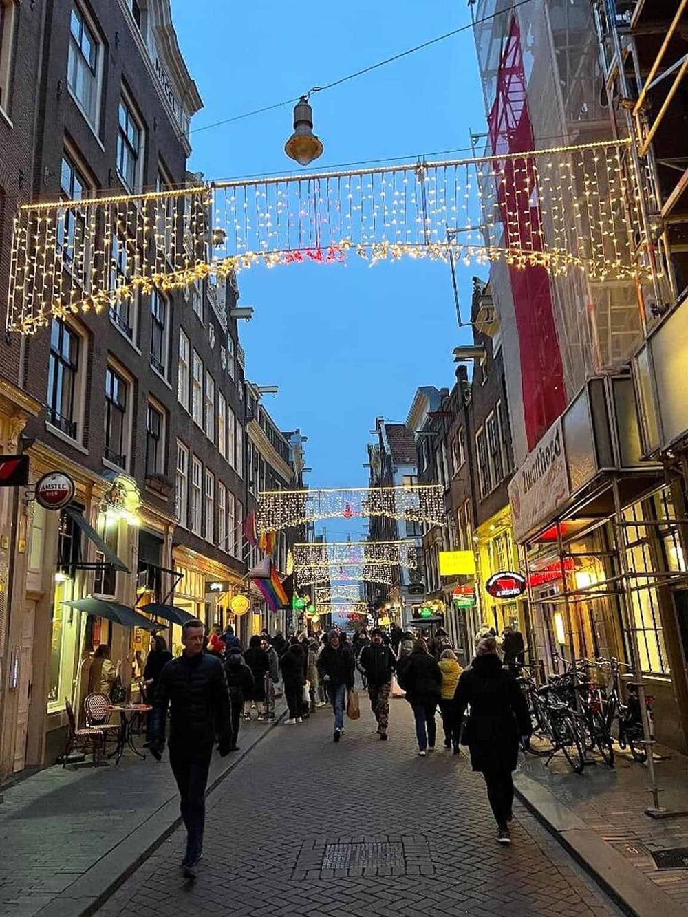 Colorful festive street decorated with lights, busy with people enjoying shopping and dining in a cityscape.
