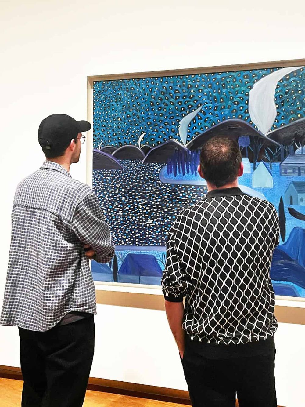 Colorful abstract art painting displayed in gallery with two visitors observing artwork.