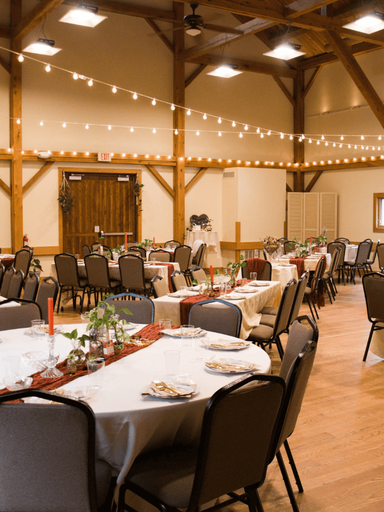 Cozy event space with decorated tables, string lights, and rustic wooden beams for weddings or celebrations.