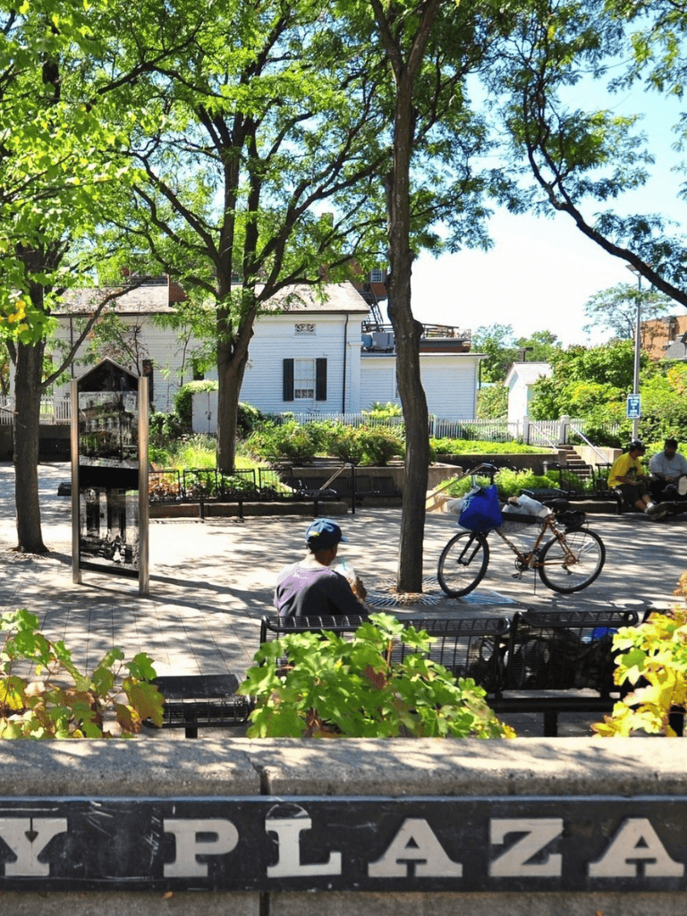 A park with trees, benches, and people relaxing on sunny day in town.