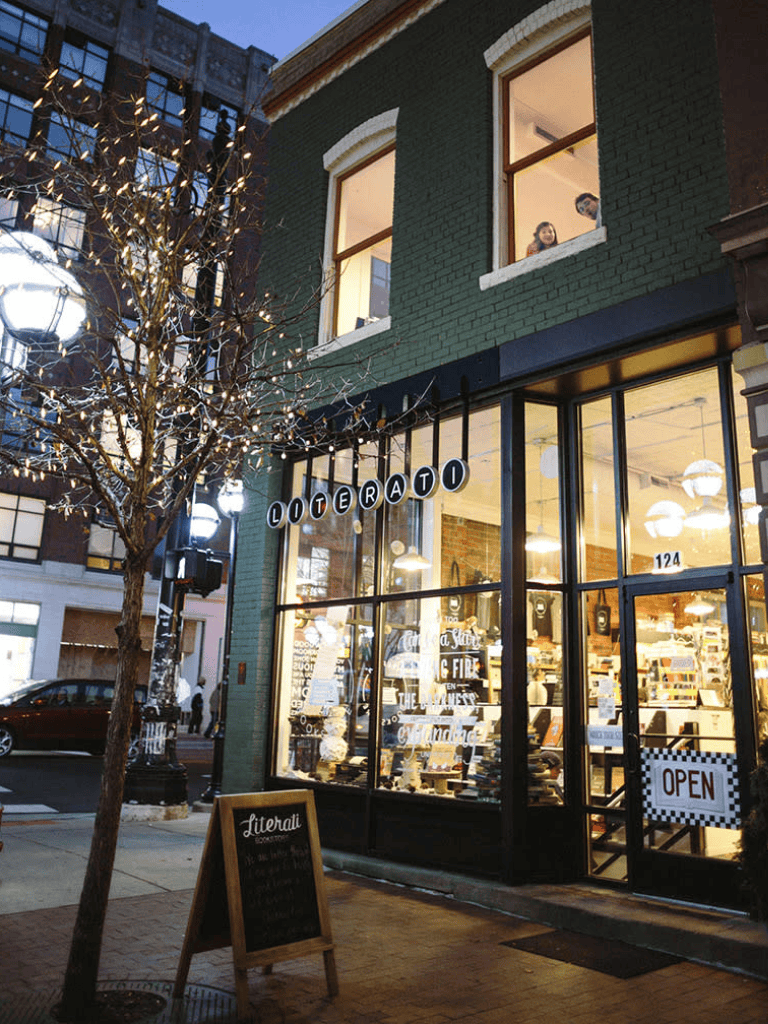 Literary bookstore storefront with illuminated display windows and outdoor chalkboard sign.
