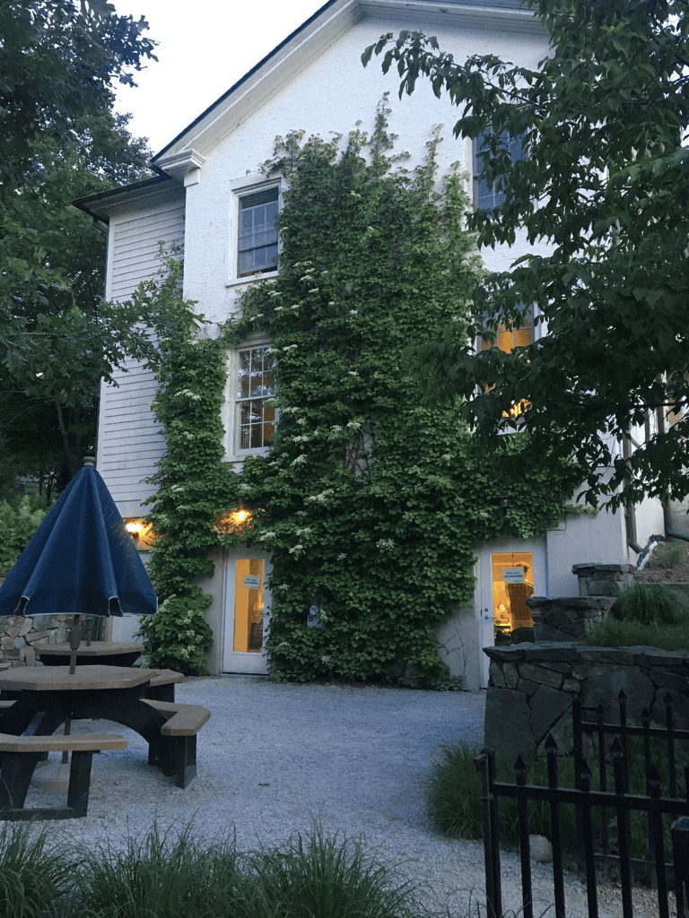 Vine-covered white house with outdoor seating and gravel pathway, inviting garden setting.